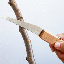 Load image into Gallery viewer, Hand holding the folding saw about to cut a tree branch